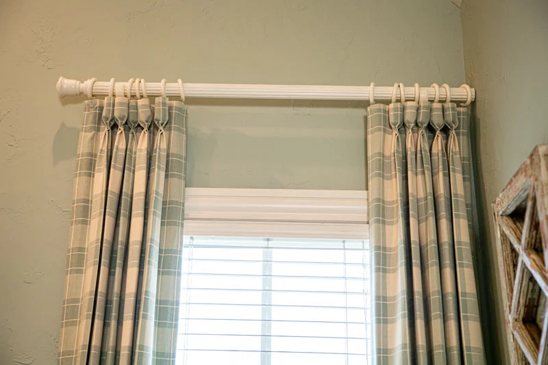 Pleated plaid draperies on a light rod above white blinds